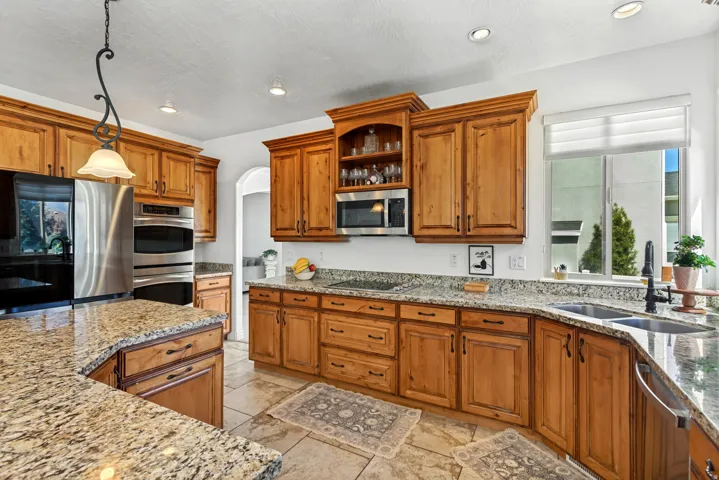 Kitchen featuring light wood cabinetry, granite-patterned countertops, stainless steel appliances, a double basin sink with a dark-finish faucet, and recessed lighting