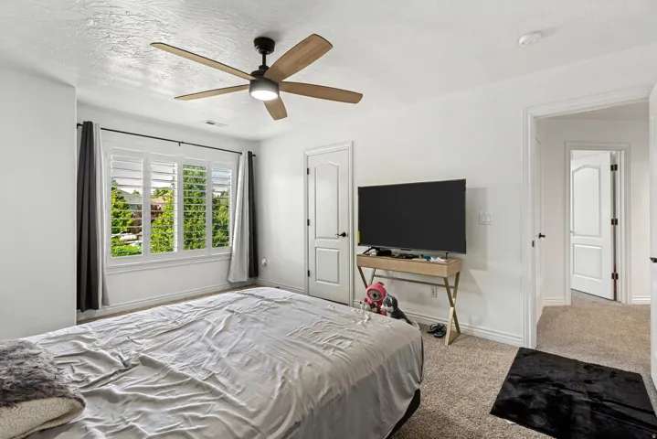Carpeted flooring, white walls, overhead ceiling fan with light, white plantation shutters, and a white interior door with black hardware
