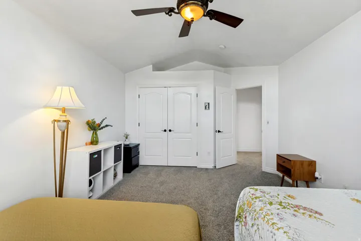 Vaulted ceiling featuring a ceiling fan with integrated lighting, carpeted flooring, and white interior doors with black hardware