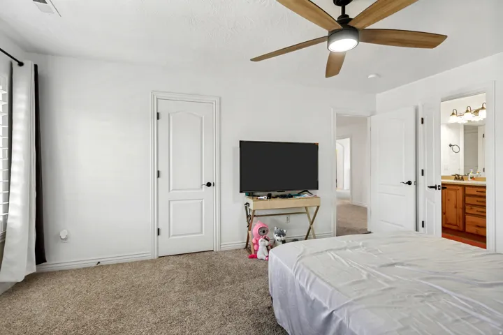 Plush carpet flooring, ceiling fan with integrated lighting, white interior doors, and a bathroom entry with dual vanity