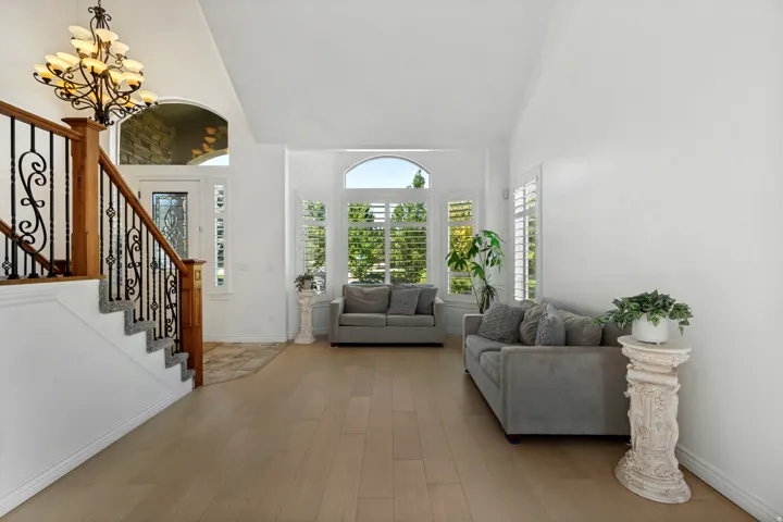 Wood-finish flooring, staircase with wrought iron balusters and wood handrail, arched windows with plantation shutters, and a chandelier with multiple light sources