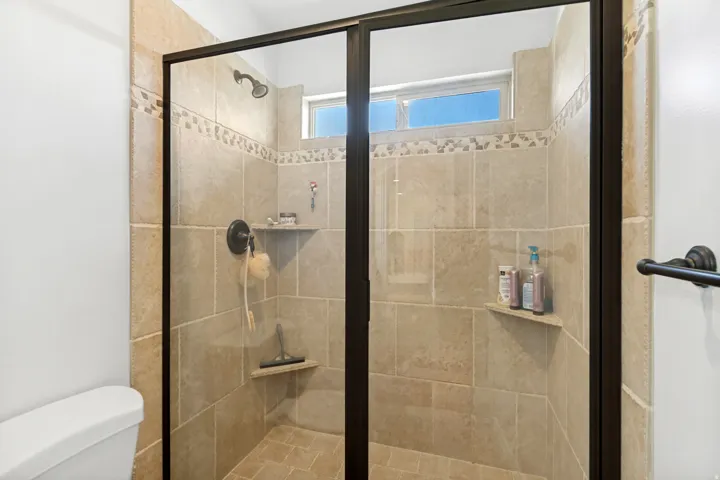 Glass-enclosed shower with a bronze-finish frame, tiled walls, and built-in shelving