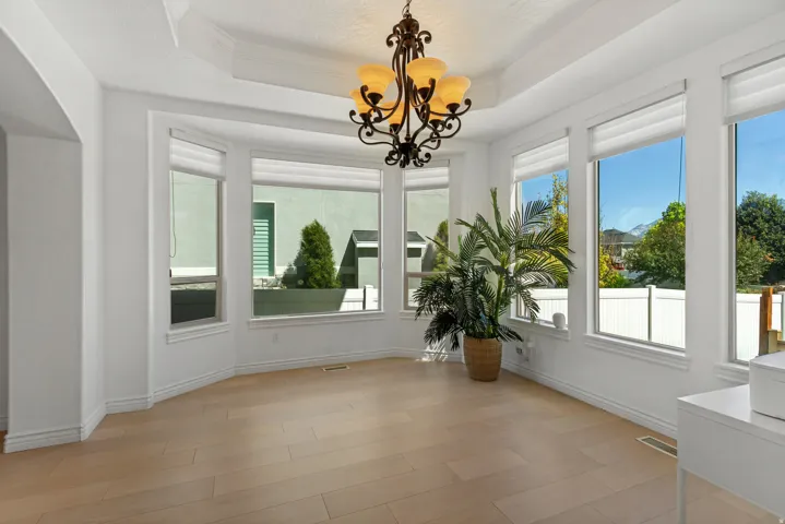 Wood-finish flooring, tray ceiling, ornamental chandelier, multiple large windows, and white window blinds