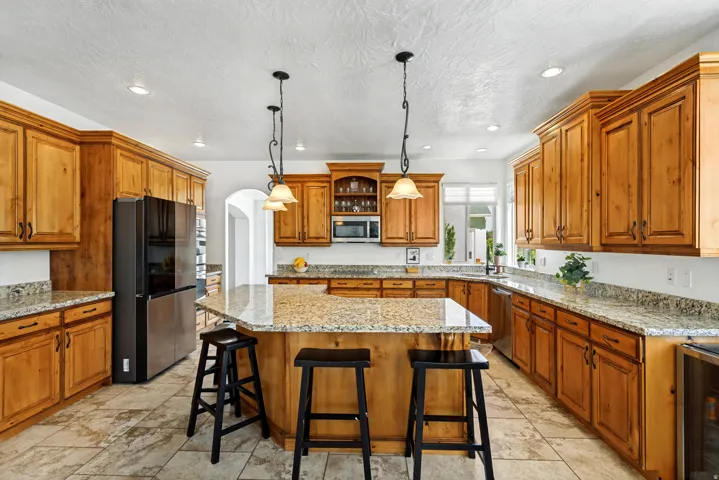 Maple cabinetry with crown molding, granite countertops, tile flooring, recessed lighting, and a kitchen island with pendant lighting