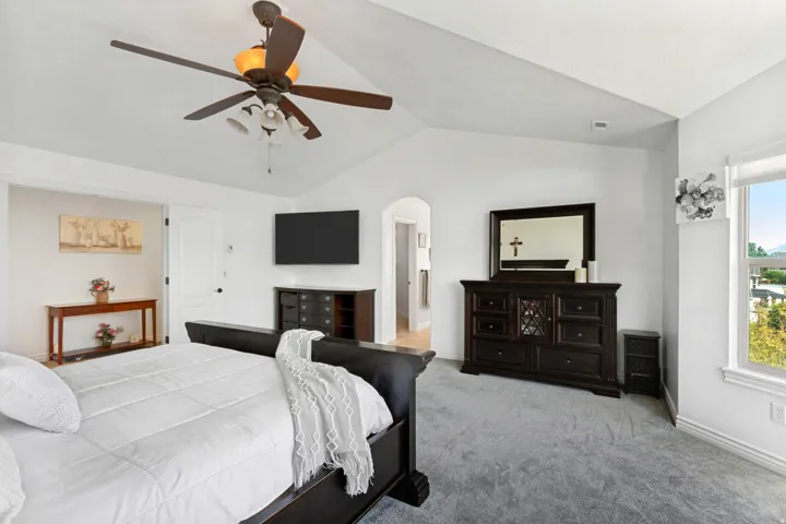 Vaulted ceiling with a ceiling fan, light gray carpeting, and an arched doorway