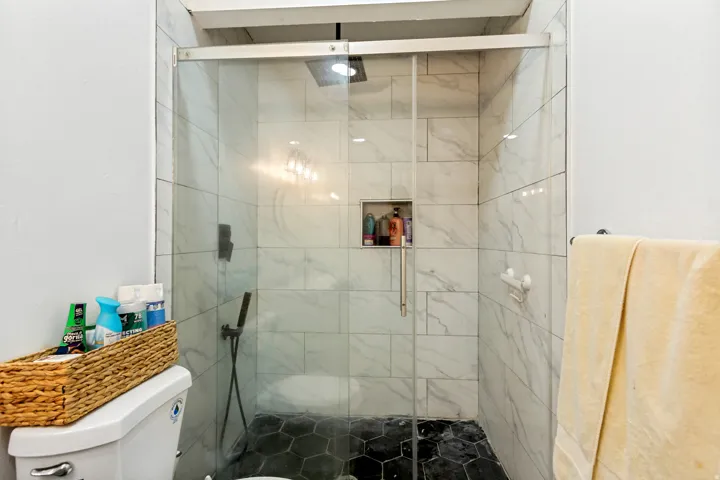 Glass-enclosed shower with white tiled walls, hexagonal black floor tiling, and a recessed shower niche
