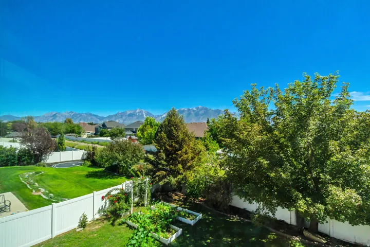 Expansive green lawn with a white privacy fence, raised garden beds, and mature trees