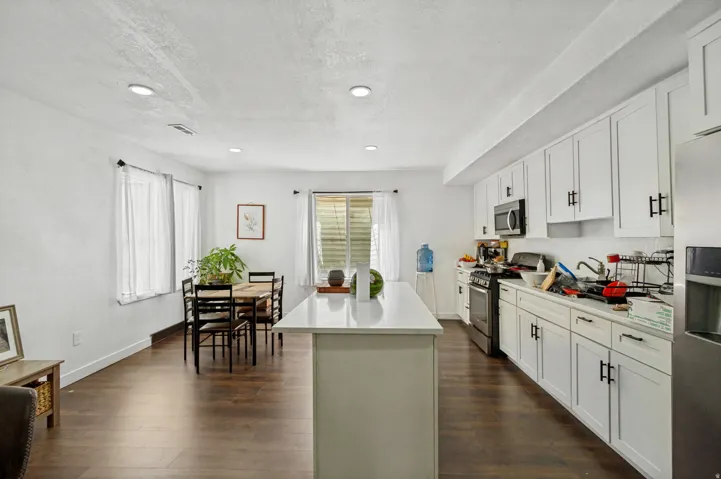Open-concept kitchen and dining area featuring dark wood-finish flooring, recessed lighting, and white cabinetry with dark hardware