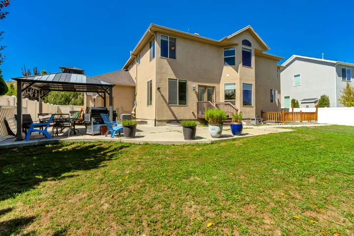Rear exterior featuring a stucco finish, two-story design, multiple windows, a ground-level patio, and a covered gazebo