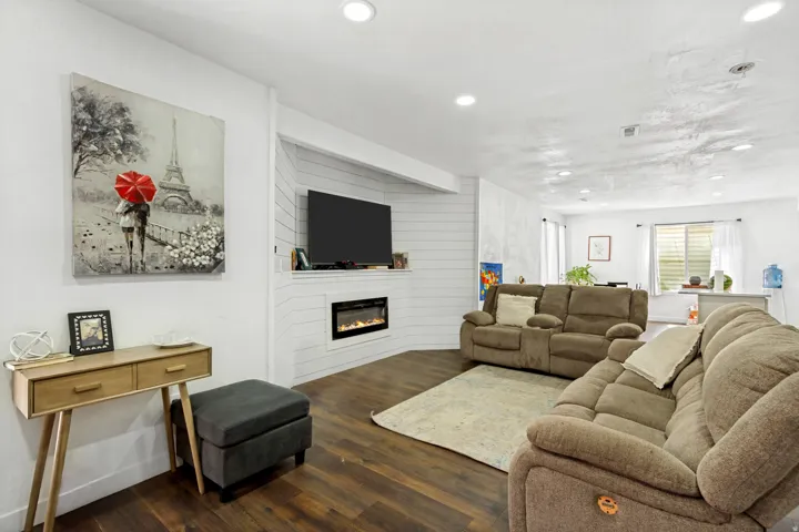 Wood-finish flooring, recessed lighting, and an electric fireplace with a shiplap surround