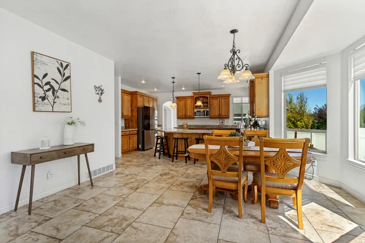 Travertine tile flooring throughout, kitchen with wood cabinetry and dark appliances, kitchen island with seating, arched doorway, bay window with blinds
