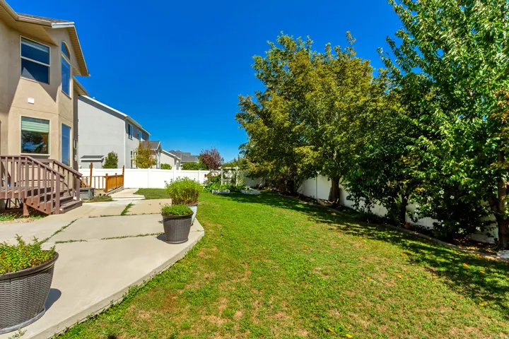 Expansive grassy yard with mature trees, concrete patio, and a privacy fence