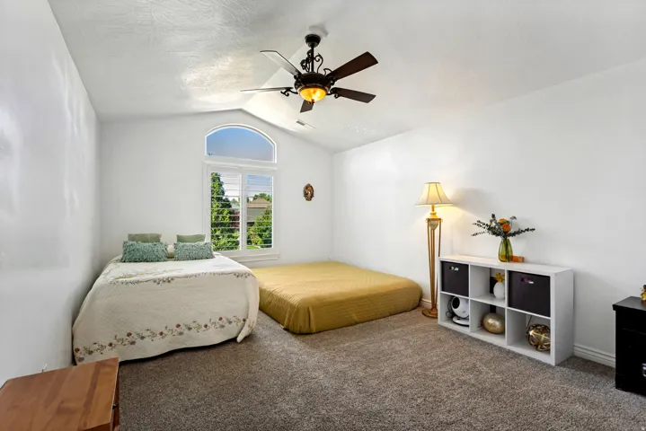 Vaulted ceiling with an attached ceiling fan, arched window with plantation shutters, and carpeted flooring