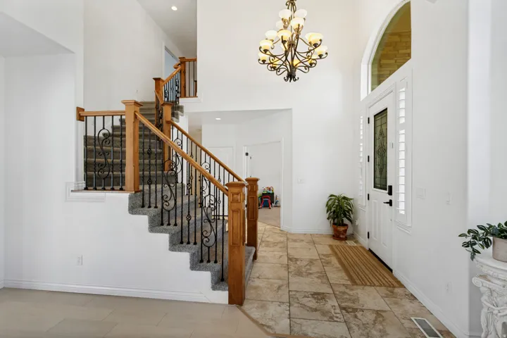 Two-story foyer featuring a grand staircase with wood newel posts and wrought iron balusters, a decorative chandelier, and an arched transom window