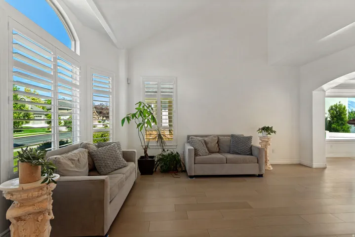 Vaulted ceilings, wood-finish flooring, white plantation shutters, arched window, and an arched entry