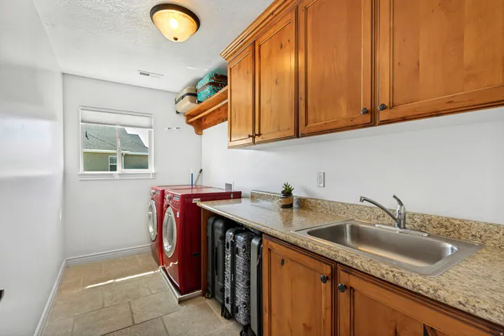 Laundry area featuring a window, built-in cabinetry, upper shelving, a sink with a faucet, and stone-finish flooring