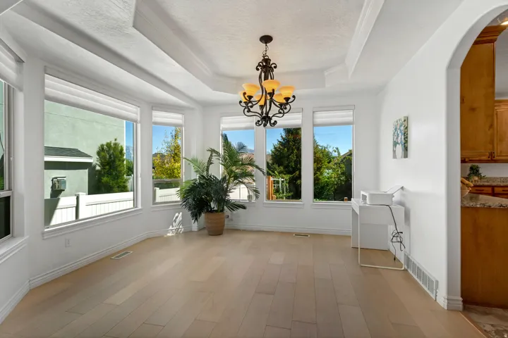 Tray ceiling with a decorative chandelier, light wood-finish flooring, and multiple windows