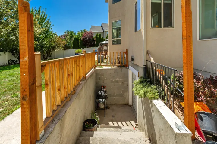 Basement entrance featuring concrete steps, concrete retaining walls, and a wooden handrail