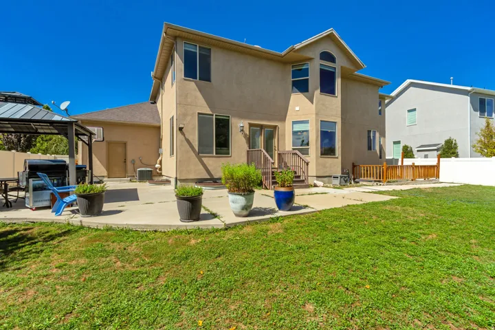 Two-story stucco exterior with multiple windows, concrete patio, grass lawn, and wood deck with railing
