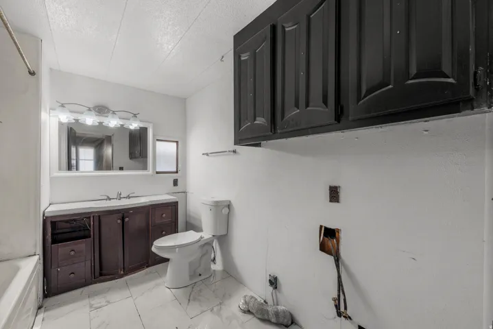 White tile flooring with grey veining, dark wood-finish vanity, mirrored medicine cabinet, and white toilet