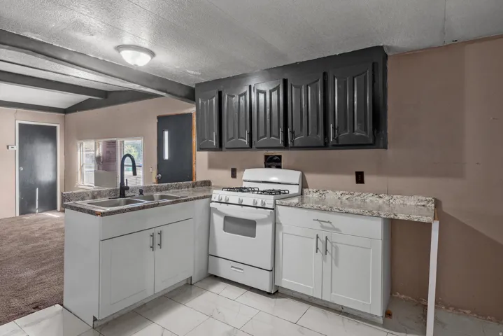 Kitchen featuring a gas range, dual basin sink with a gooseneck faucet, white base cabinetry, dark wall cabinetry, and light-toned countertops