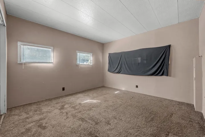 Carpeted flooring with light-toned walls, two windows with blinds, and an exposed ceiling