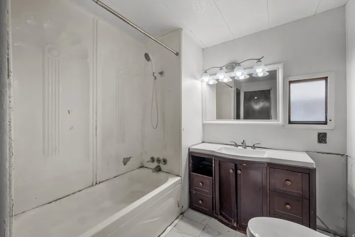 Built-in bathtub with shower, dark wood-finish vanity, integrated sink, wall-mounted mirror, and vanity light fixture
