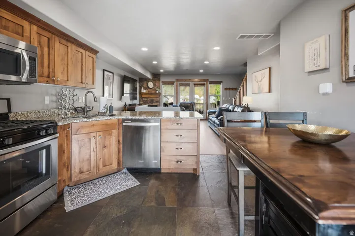 Kitchen featuring stainless steel appliances, wood cabinetry, stone countertops, and a built-in island