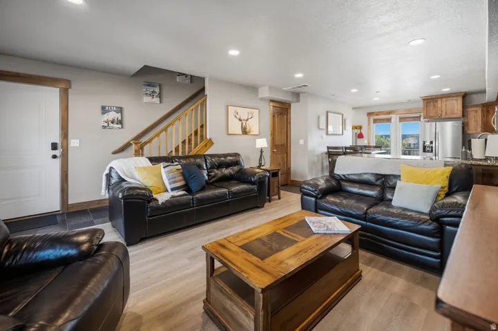 Open-concept living area with wood-finish flooring, recessed lighting, wood-trimmed windows, and a staircase with wood railings