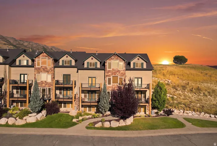Multi-level residences featuring stone and siding exteriors, private balconies with metal railings, and a landscaped front yard with a paved walkway