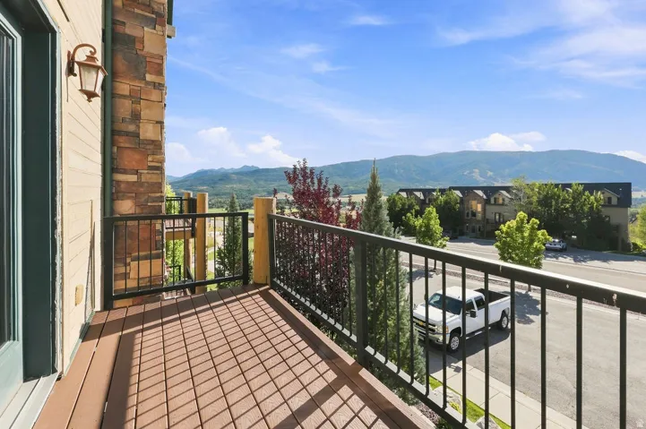 Private balcony with composite decking, decorative metal railing, and a stone facade exterior