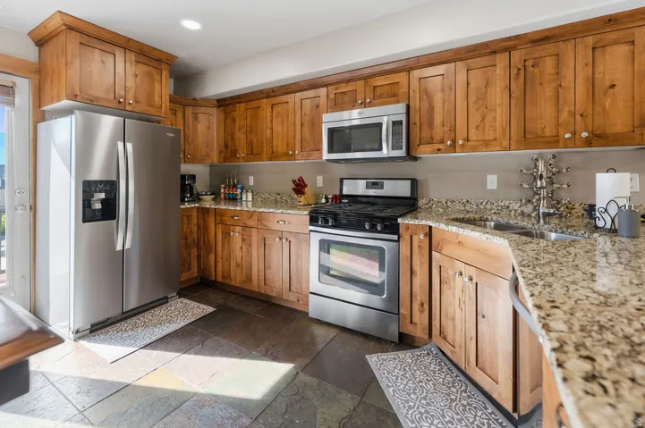 Kitchen featuring extensive wood cabinetry, stainless steel appliances, speckled countertops, and stone tile flooring