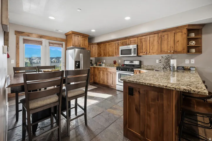 Kitchen featuring wood cabinetry, stainless steel appliances, granite countertops, and slate tile flooring