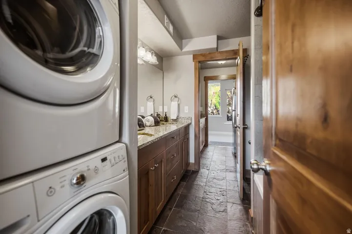Integrated laundry appliances, dual vanity with granite countertop, wood-finish cabinetry, and stone-finish flooring