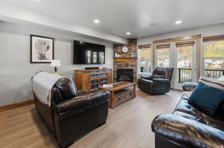 Living area featuring wood-finish flooring, recessed lighting, a stone-clad fireplace with a wood mantle, and double glass doors opening to an outdoor space