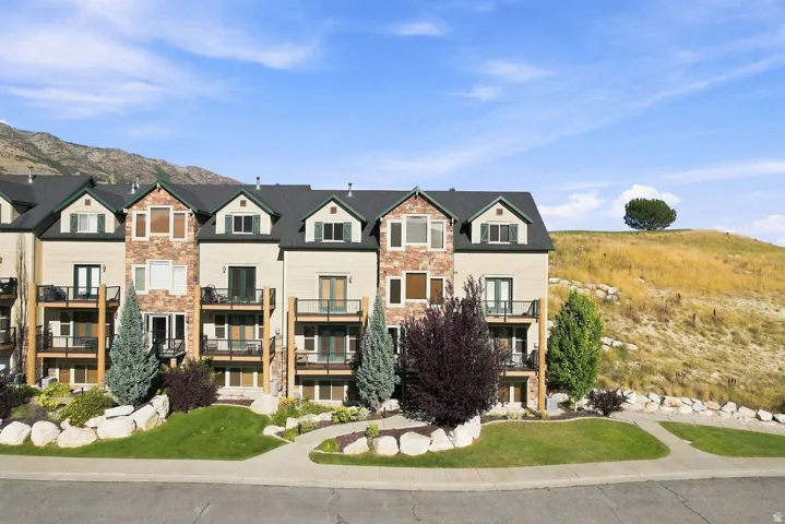 Multi-level townhome exterior featuring stone and siding finishes, individual balconies, and a paved walkway