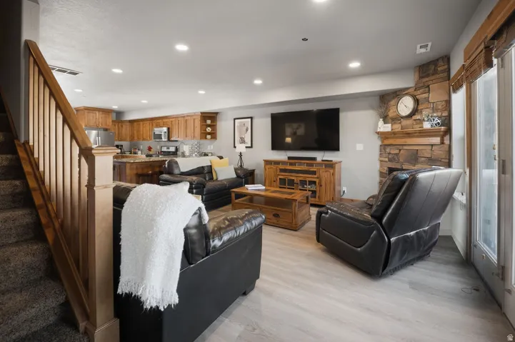 Open-concept living area with wood-finish flooring, stone-clad fireplace with wood mantel, and recessed lighting