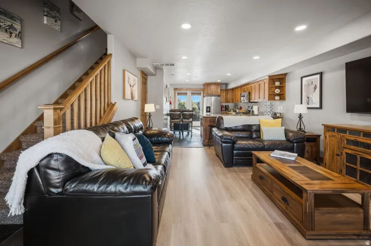 Open-concept living area with wood-finish flooring, recessed lighting, and a staircase with wood railing
