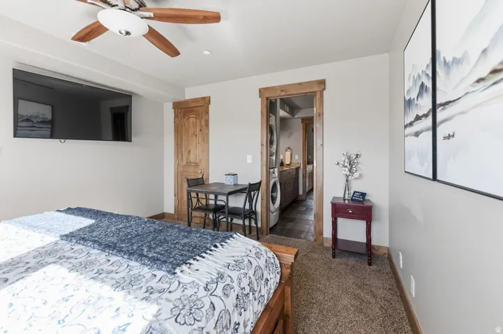Wood-finish ceiling fan, wall-mounted television, and a separate built-in laundry area with stacked appliances