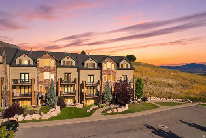 Multi-level townhome architecture with dormer windows, stone and siding exterior, multiple private balconies, and an established landscaped entrance