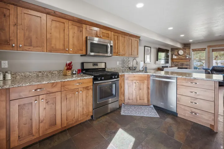 Wood-finish cabinetry, stone flooring, stainless steel appliances, recessed lighting, and stone countertops