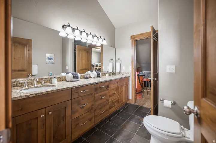Dual vanity with granite countertop, integrated sinks, wood cabinetry, and a large mirror with overhead lighting