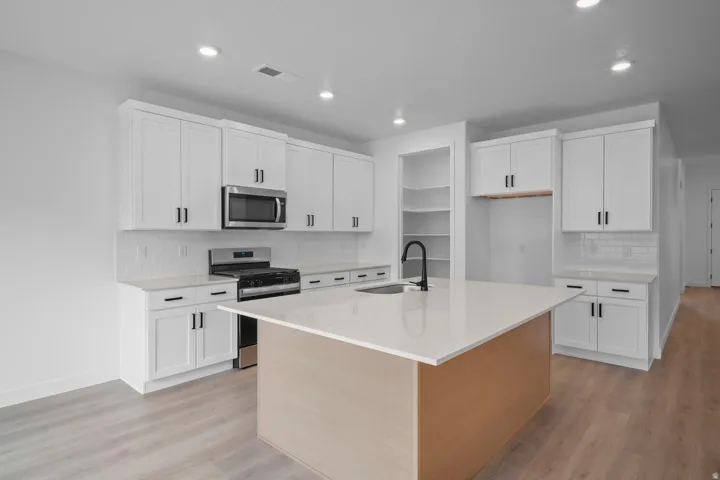 White shaker cabinetry, stainless steel appliances, central island with light-toned wood paneling, light countertop, and light wood-finish flooring