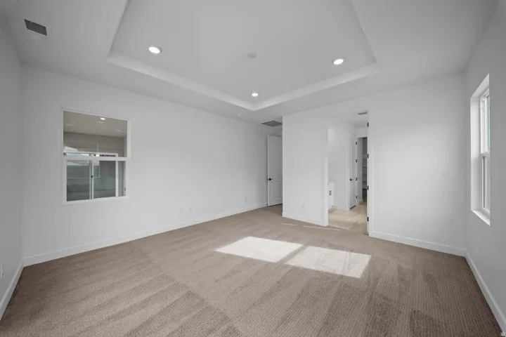 Recessed lighting, tray ceiling, two windows, two white doors, and carpet flooring