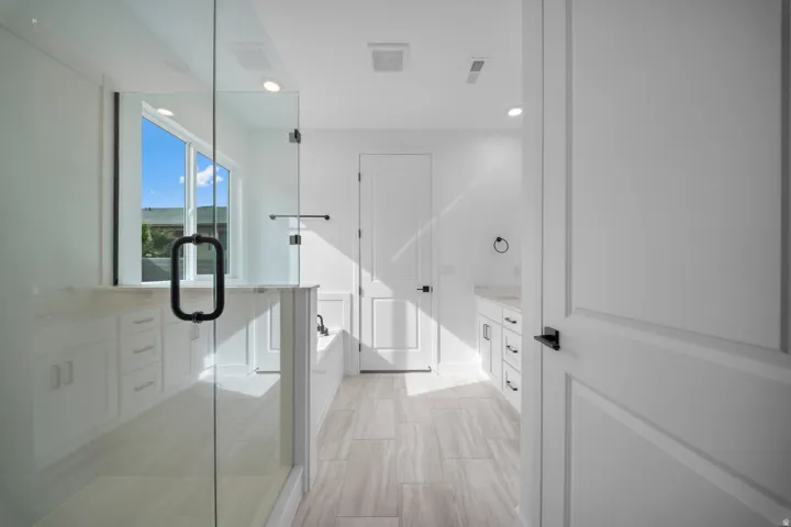 Spacious bathroom featuring a glass-enclosed shower, built-in soaking tub, dual vanity with undermount sinks, and light-toned tile flooring