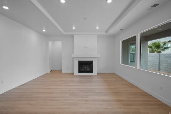 Recessed lighting, tray ceiling, integrated fireplace with mantel, horizontal shiplap accent wall, and wood-finish flooring