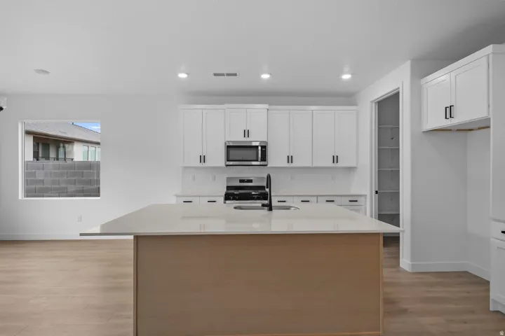 Open-concept kitchen featuring an island with a light-toned countertop, white cabinetry with dark hardware, stainless steel appliances, and wood-finish flooring
