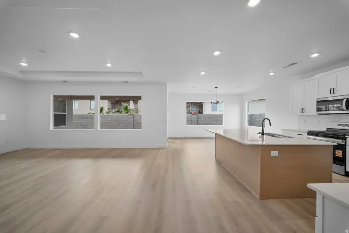 Open-concept living space featuring wood-finish flooring, recessed lighting, and a kitchen island with an undermount sink and matte black faucet