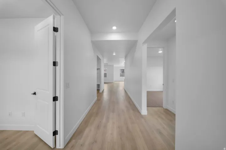 Elongated hallway with wood-finish flooring, recessed lighting, and white paneled doors with matte black hardware