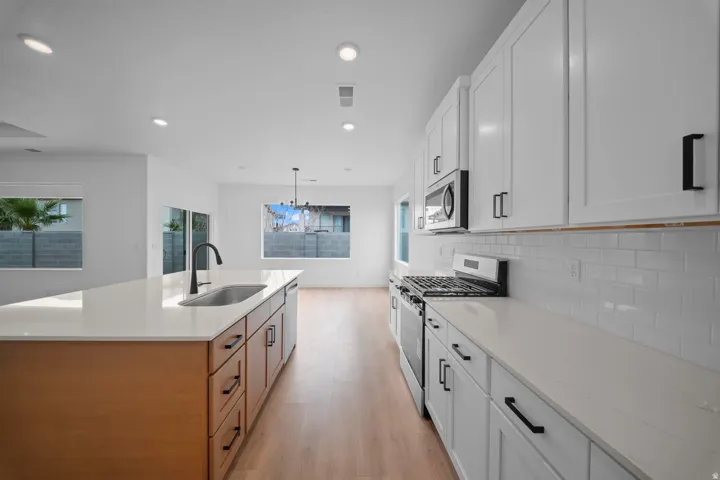 White shaker cabinetry, quartz countertops, stainless steel appliances, wood-finish flooring, and recessed lighting